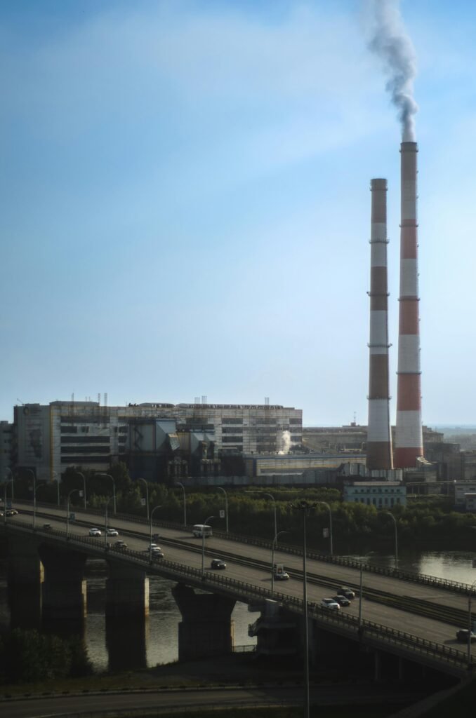 A factory with smoke stacks near a bridge over a river, showcasing industrial pollution.