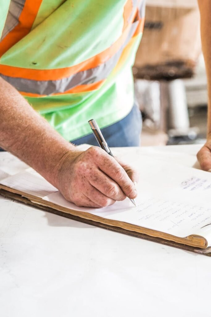 A construction worker writes notes on a clipboard at a construction site, emphasizing planning and precision.